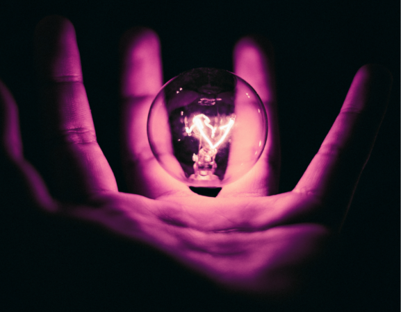 Close up of an open palm holding an illuminated light bulb.